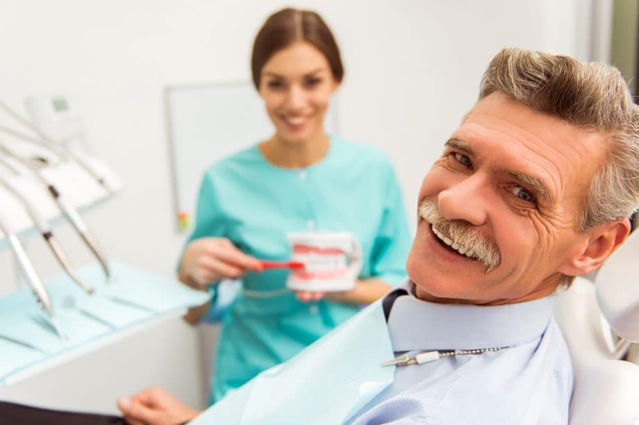 Older man and female hygienist smiling in dental exam room