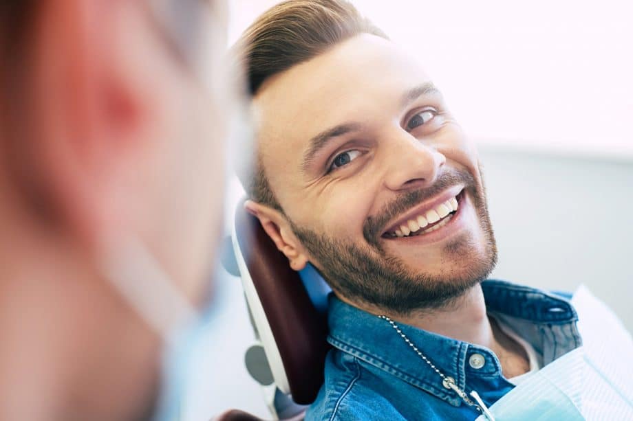 Man smiling up at dentist while sitting in dental exam room chair